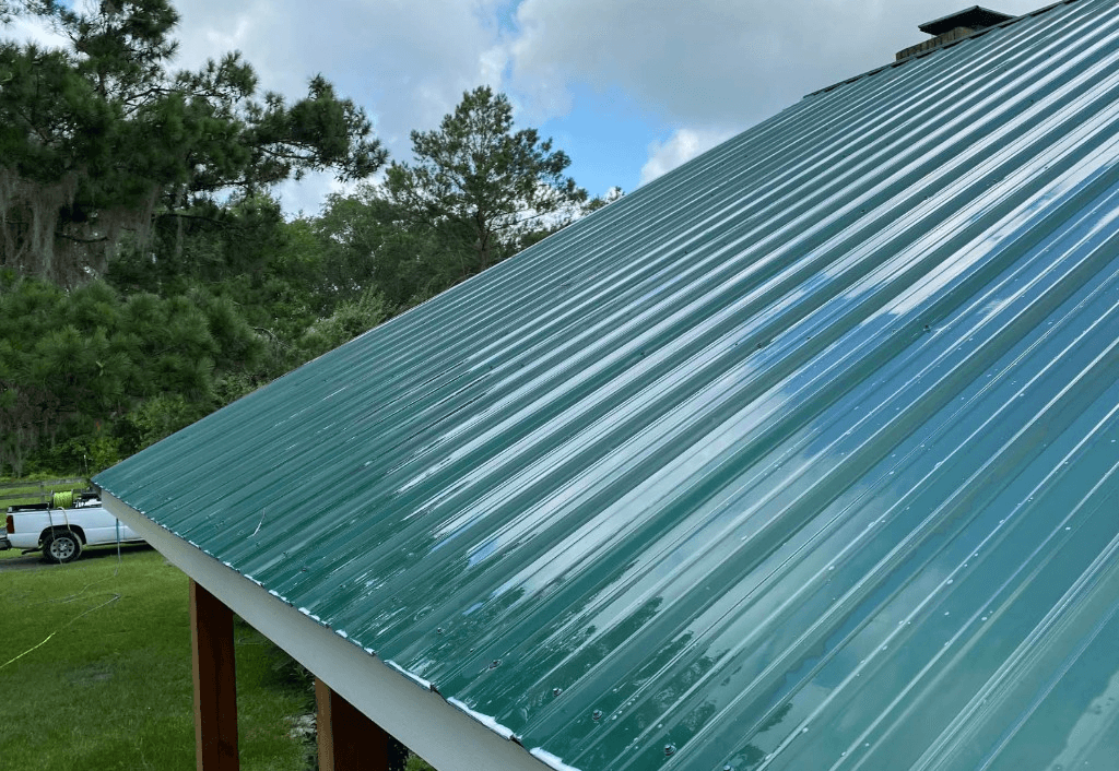 Green metal roof being soft washed with soap foam and equipment visible